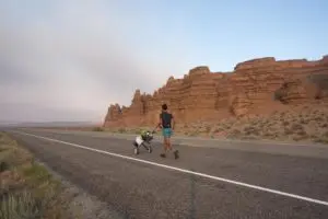 A photo of a man running down a road wheeling his possessions 