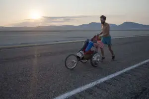 A photo of a man running down a road wheeling his possessions 