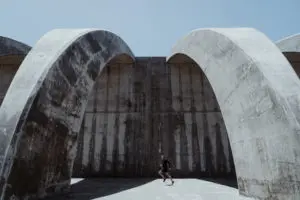A photo of a concrete building with a man running in front of it