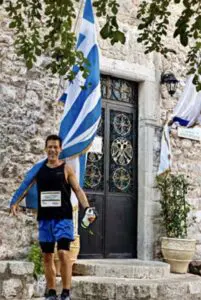 A photo of a man in running attire holding a large Greek flag