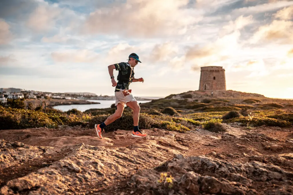 A photo of a man running on rocks with some water in the background