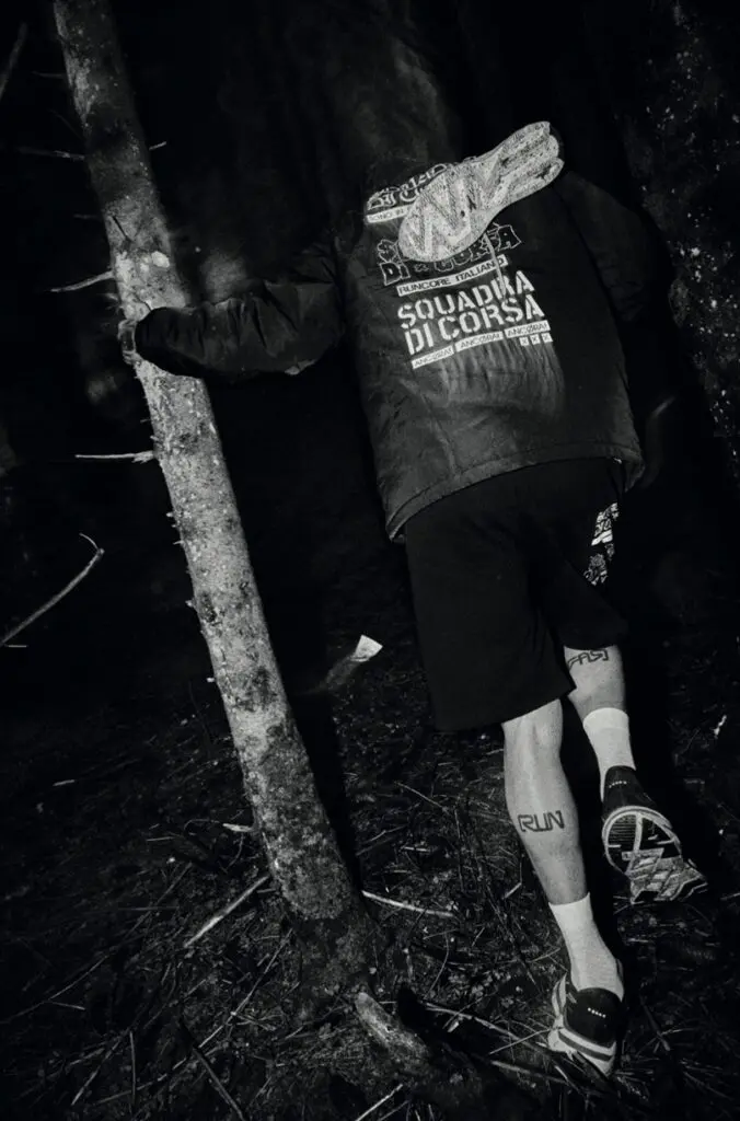 A black and white photo of someone leaning against a tree in the dark