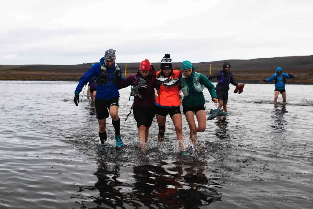 A photograph of five women helping each other out wading through water