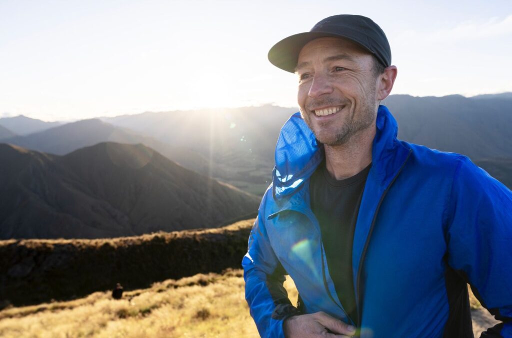 A close up of a man smiling with a mountainous backdrop